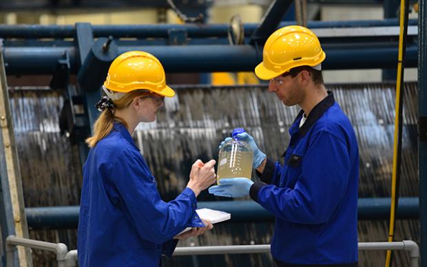 Two individuals in blue work uniforms conducting wastewater surveillance in an outdoor setting. 