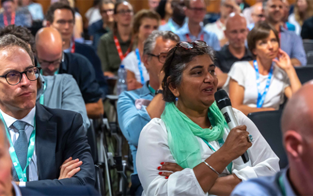 woman talking in a microphone surrounded by peoole in a public event