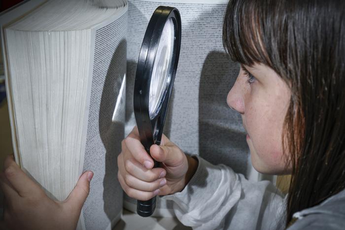 Girl reading a book with a magnifying glass