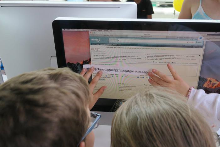 Two children comparing a paper DNA sequence with a website