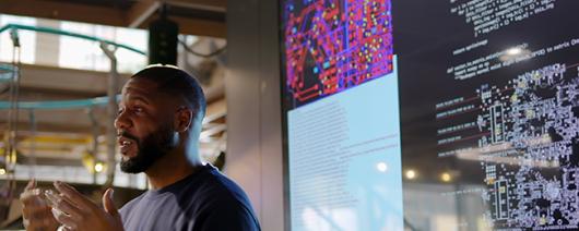 Close up stock photograph of a black man conducting a seminar on Python computer coding in an open plan work arena