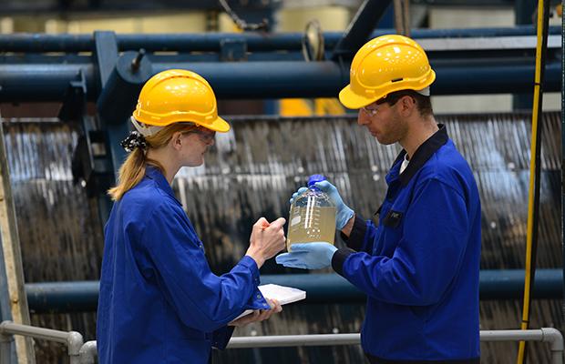 Two individuals in blue work uniforms conducting wastewater surveillance in an outdoor setting. 