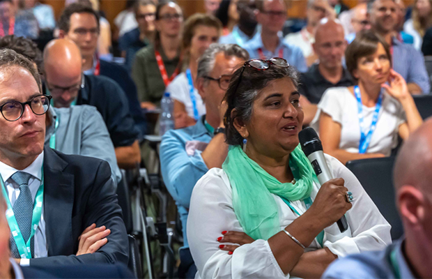 woman talking in a microphone surrounded by peoole in a public event